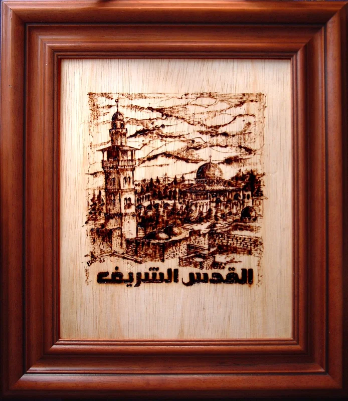 A framed architectural scene on a pale wood-grain panel, with Arabic lettering reading al-Quds al-Sharif.